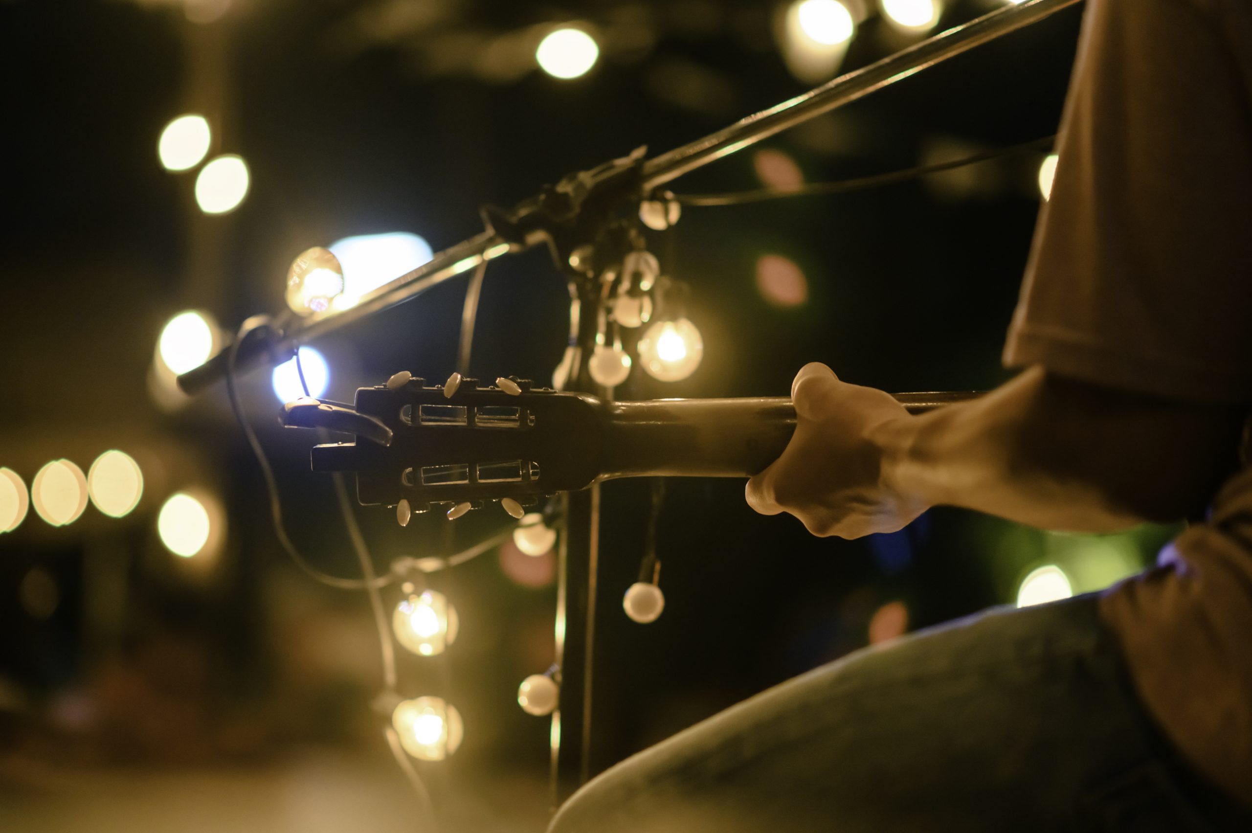 Rear view of the man sitting play acoustic guitar on the outdoor concert with a microphone stand in the front, musical concept. concert-animation-lesuroit
